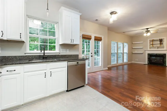 a kitchen with granite countertop a stove a sink and white cabinets with wooden floor