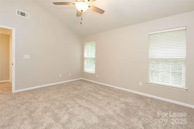 an empty room with a chandelier fan and windows