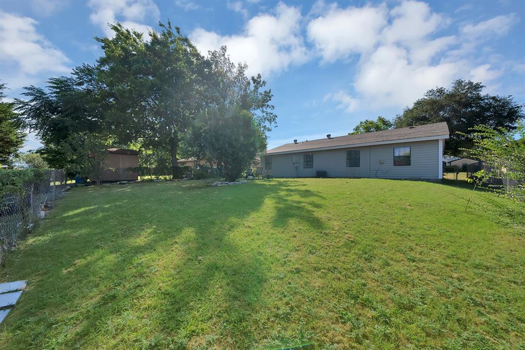 9519 County View Road Dallas, TX 75249 - Photo 21 of 31 Expansive green lawn with mature trees and a detached shed, bordered by a chain-link fence