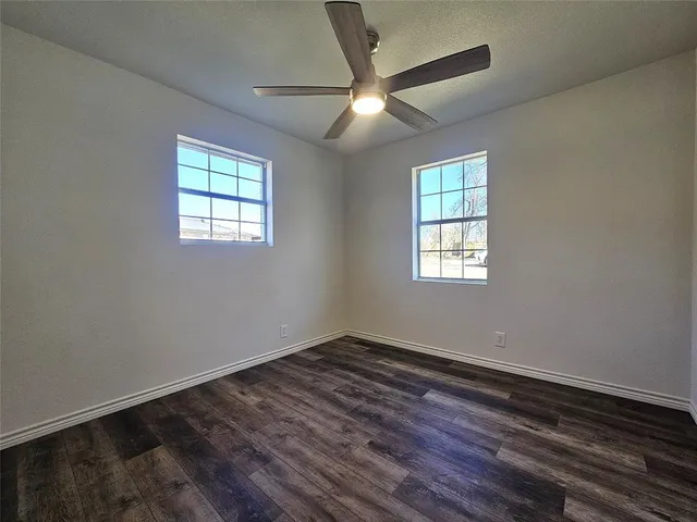 an empty room with wooden floor ceiling fan and windows