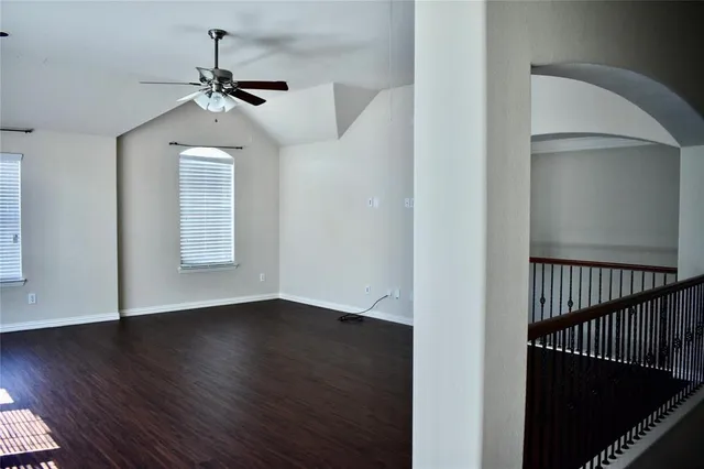 an empty room with wooden floor chandelier fan and windows
