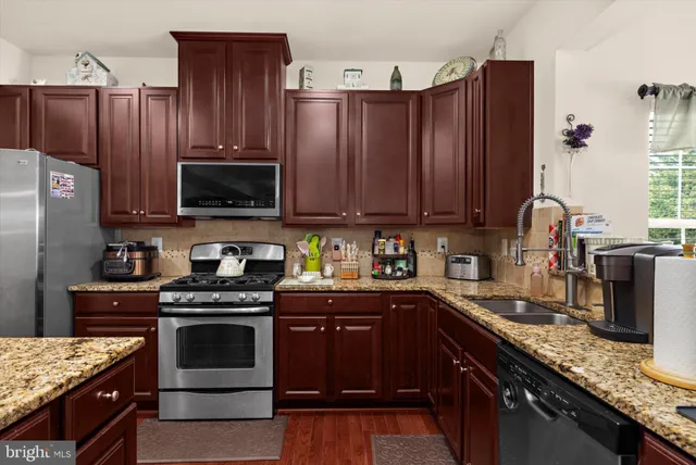 a kitchen with granite countertop stainless steel appliances a refrigerator a stove a dining table and chairs with wooden floor