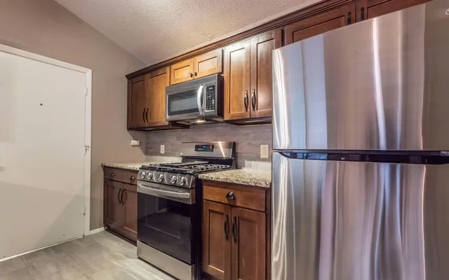 a kitchen with stainless steel appliances granite countertop a refrigerator a stove and a sink with wooden cabinets