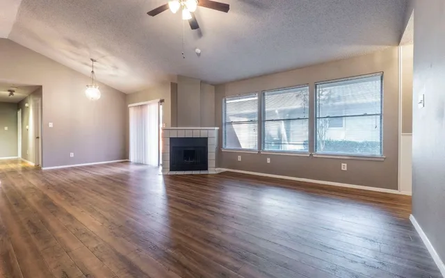 an empty room with wooden floor fireplace and windows