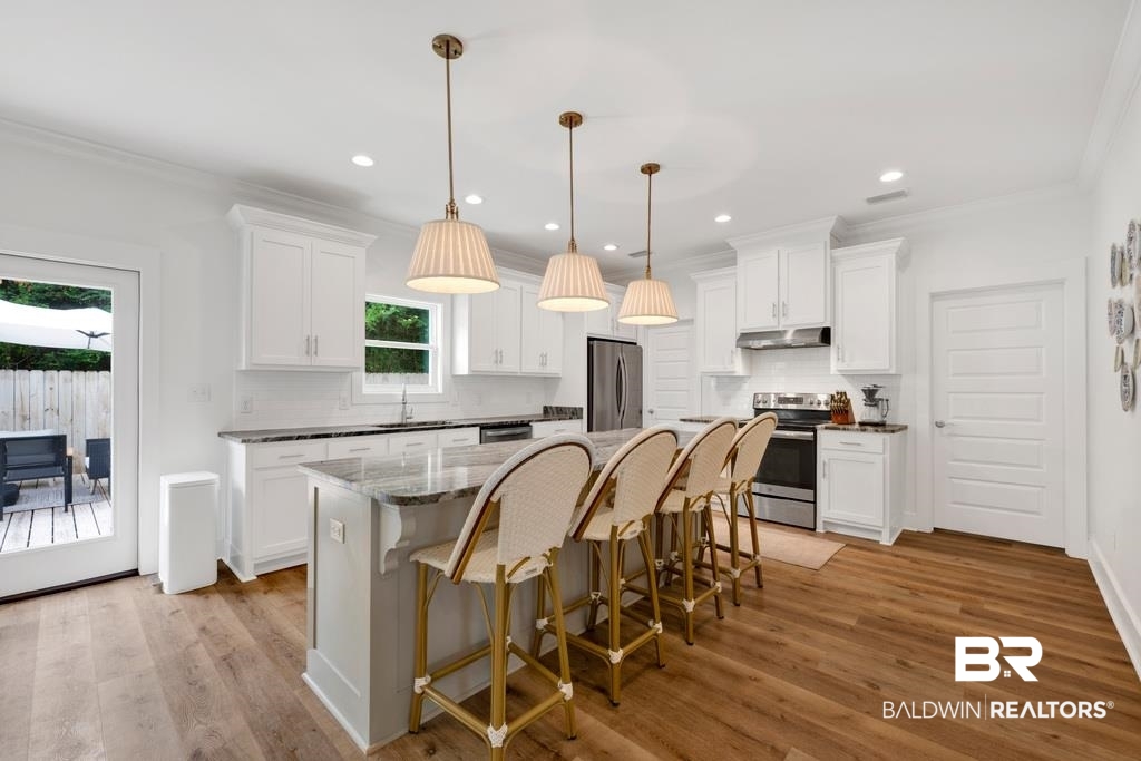 379 Pecan Ridge Boulevard Fairhope, AL 36532 - Photo 5 of 21 Bright kitchen featuring a central island with seating, white shaker cabinetry, stainless steel appliances, and wood-finish flooring
