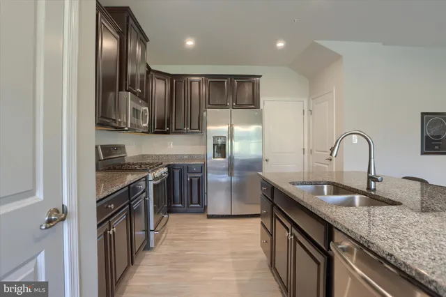 a kitchen with stainless steel appliances granite countertop a refrigerator a stove and a sink with wooden floor