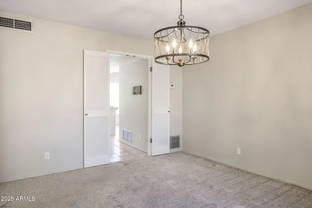 an empty room with a chandelier fan and wooden floor
