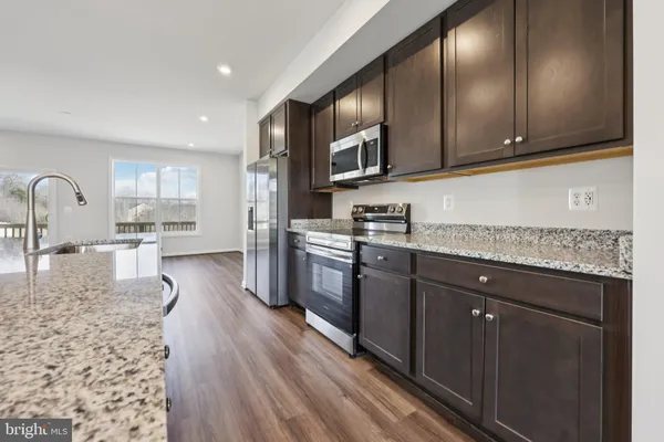 a kitchen with stainless steel appliances kitchen island granite countertop a refrigerator a sink and wooden floors