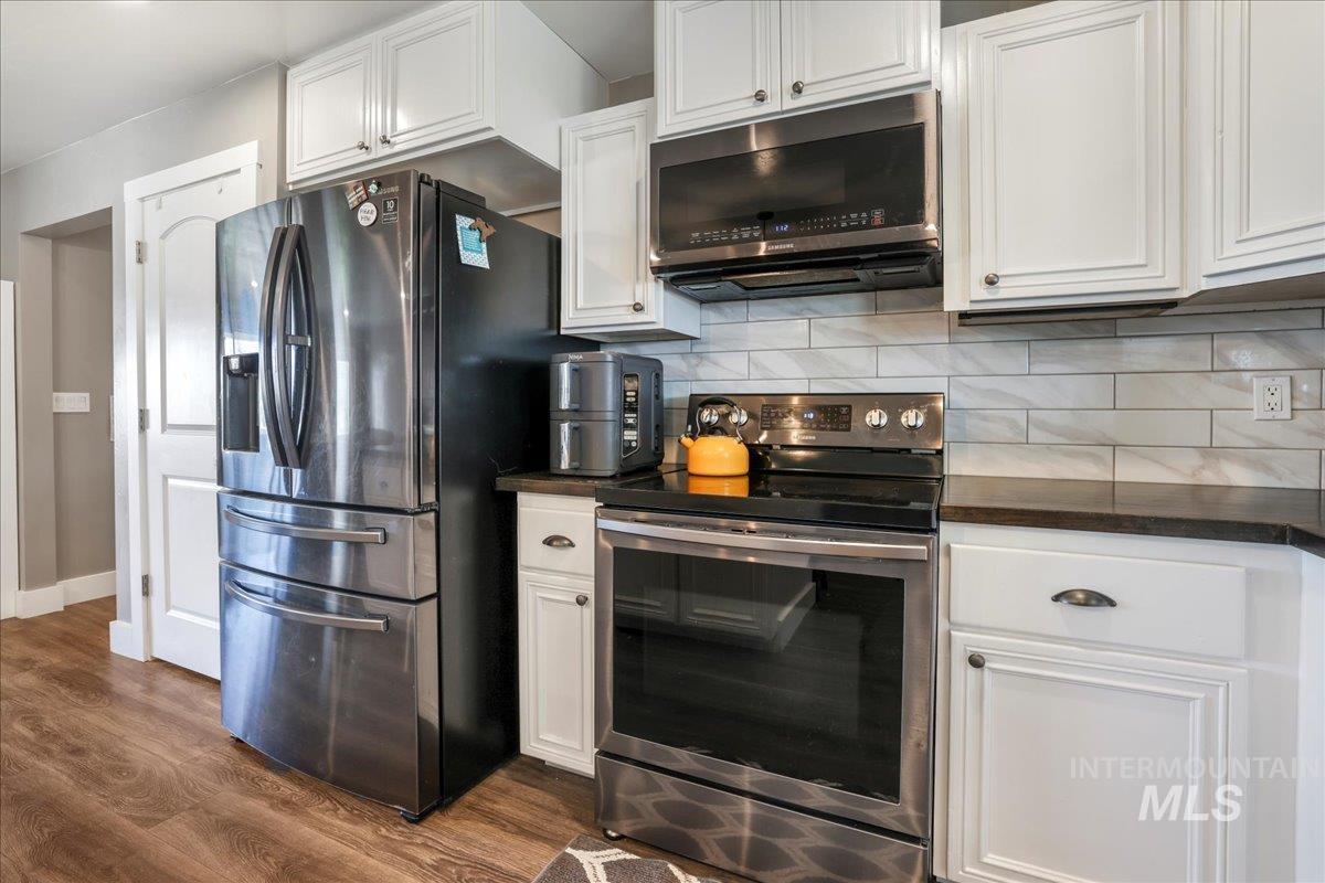4076 North 3446 East Kimberly, ID 83341 - Photo 11 of 45 Kitchen featuring appliances with stainless steel finishes, dark countertops, dark wood finished floors, white cabinetry, and decorative backsplash