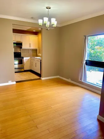 a view of empty room with wooden floor and kitchen view