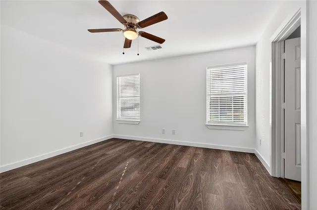 an empty room with wooden floor ceiling fan and windows