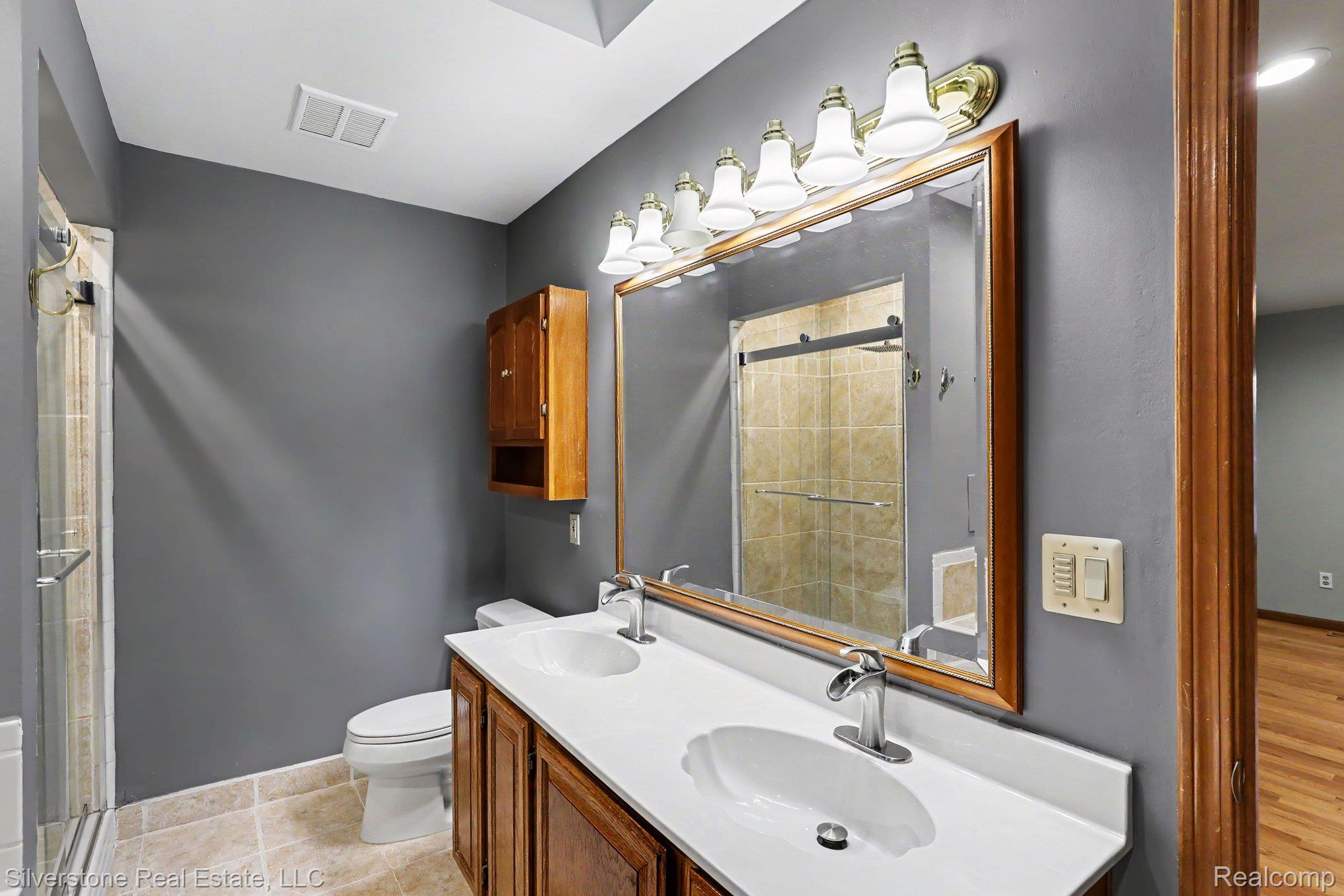 869 Timberline Drive Rochester, MI 48309 - Photo 13 of 29 Dual vanity with integrated sinks, wood cabinetry, and a large framed mirror with overhead lighting