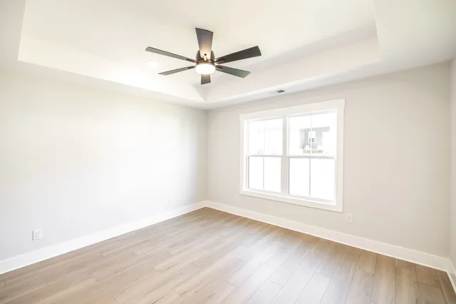 an empty room with wooden floor fan and windows