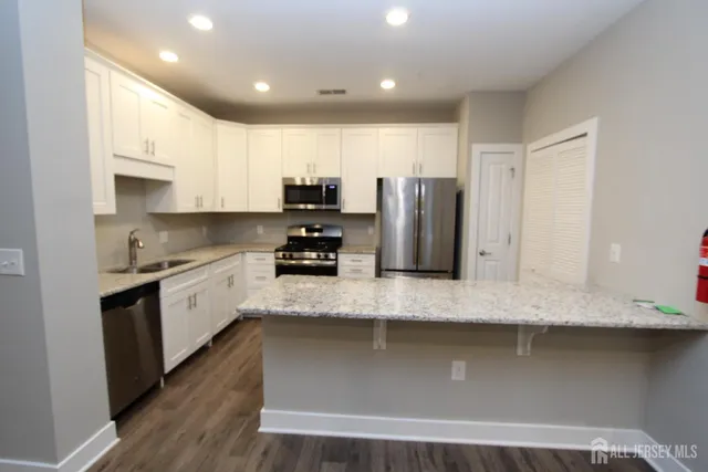 a large kitchen with stainless steel appliances granite countertop a stove a sink a refrigerator and white cabinets with wooden floor