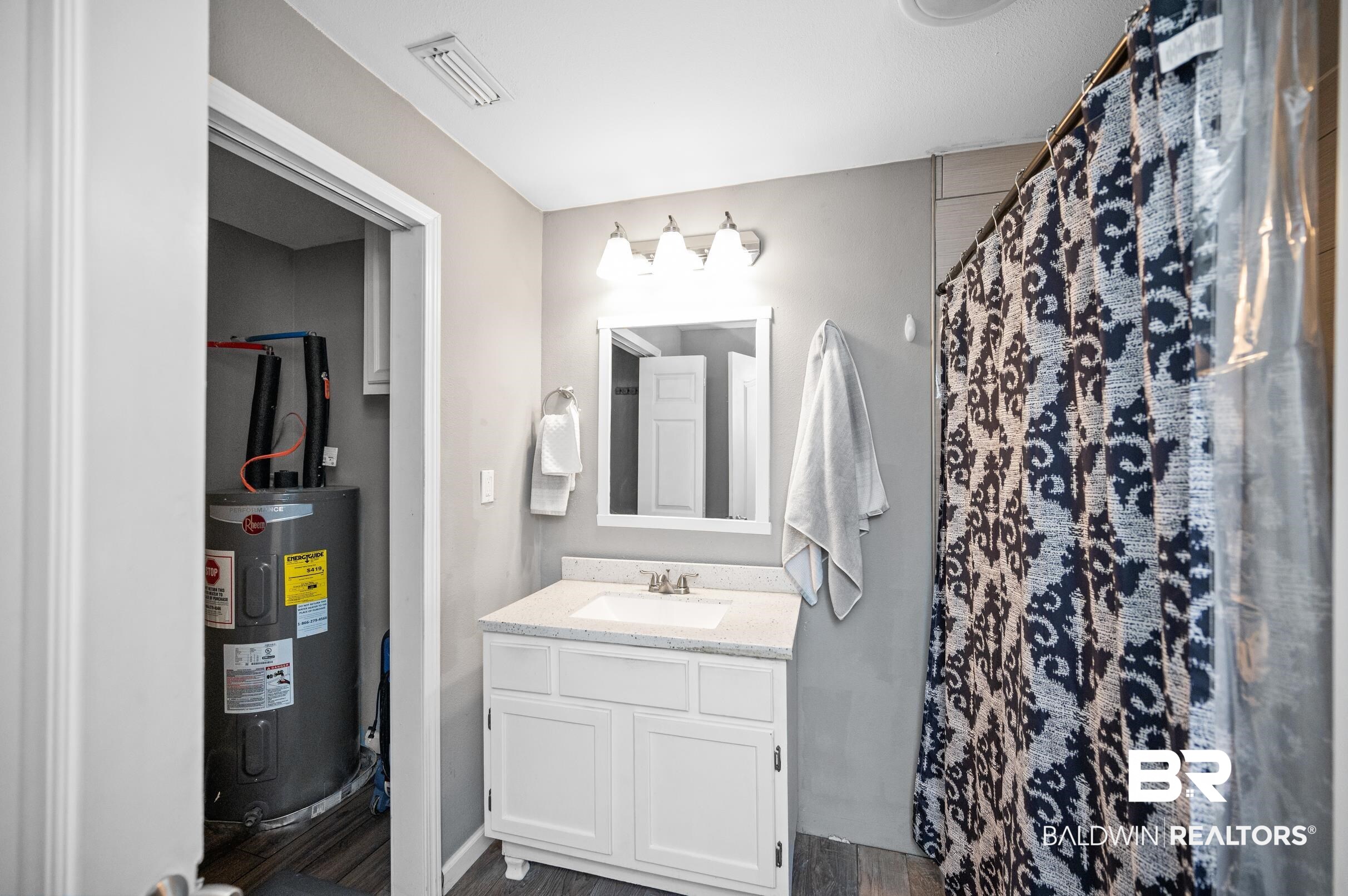 906 North Cedar Street Foley, AL 36535 - Photo 14 of 24 Bathroom with water heater, vanity, a shower with shower curtain, and hardwood / wood-style flooring