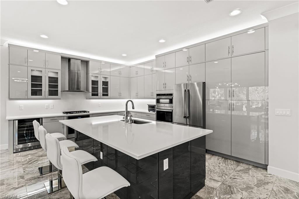 12033 Azalea Way Naples, FL 34120 - Photo 5 of 46 Sleek Euro cabinetry, extended upper cabinets, natural gas cooktop with stainless steel vent hood, a Thermador refrigerator, dual ovens, quartz counters and backsplash, plus wine fridge.