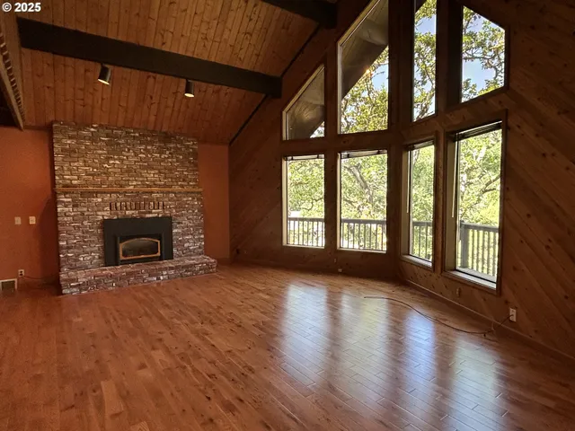 an empty room with wooden floor fireplace and windows