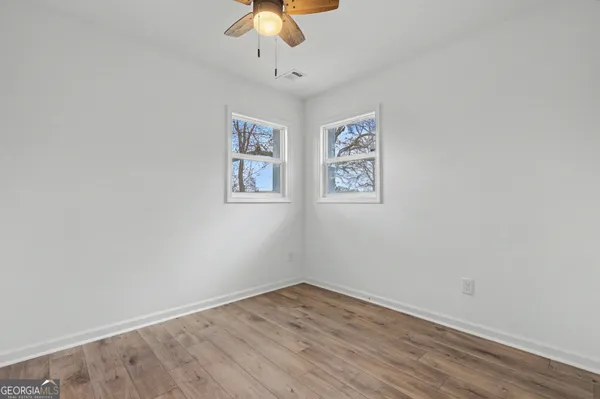 a view of an empty room with wooden floor a ceiling fan