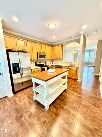 a room with stainless steel appliances a stove a refrigerator a sink a dining table and chairs with wooden floor