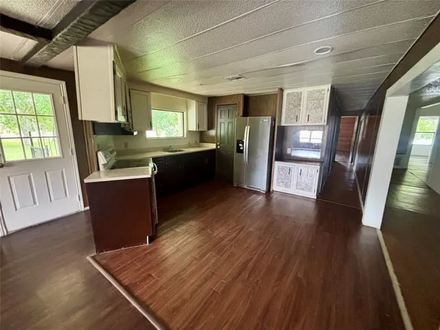 a kitchen with stainless steel appliances granite countertop a refrigerator a sink dishwasher a stove and white countertops with wooden floor