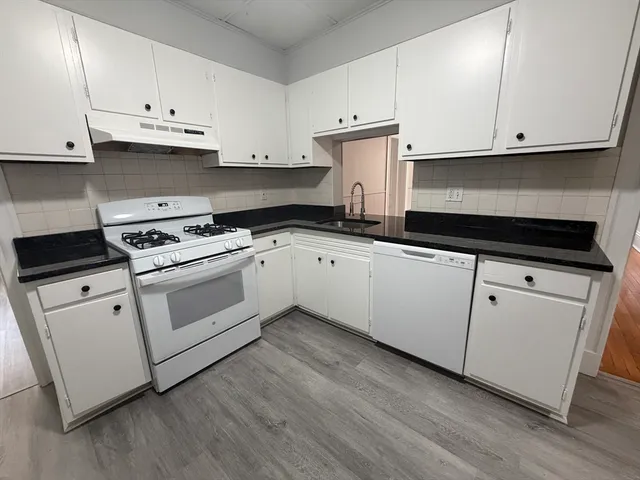 a kitchen with granite countertop white cabinets and a stove with wooden floor