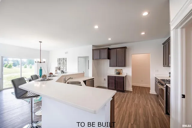 a large kitchen with stainless steel appliances a large counter top a stove a refrigerator white cabinets and wooden floor