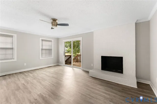 an empty room with wooden floor fireplace and windows