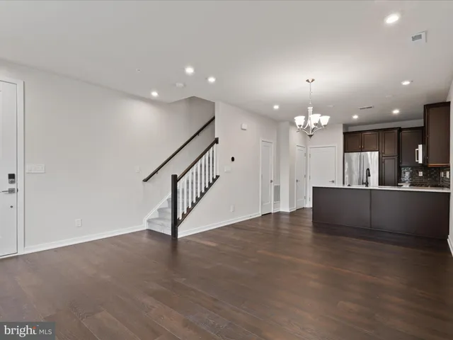 a view of an empty room with kitchen view and wooden floor