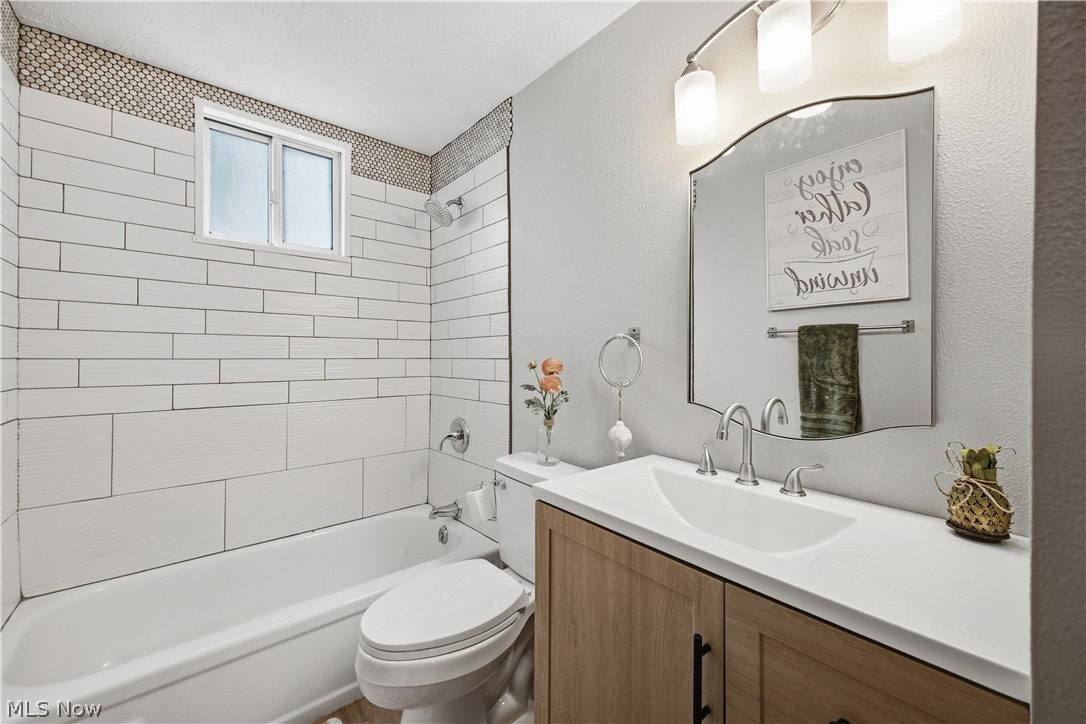 4845 New Road Austintown, OH 44515 - Photo 18 of 40 Bathroom featuring a white subway tile shower surround with a decorative mosaic accent, a window, a single vanity with wood-finish cabinetry, and a framed mirror