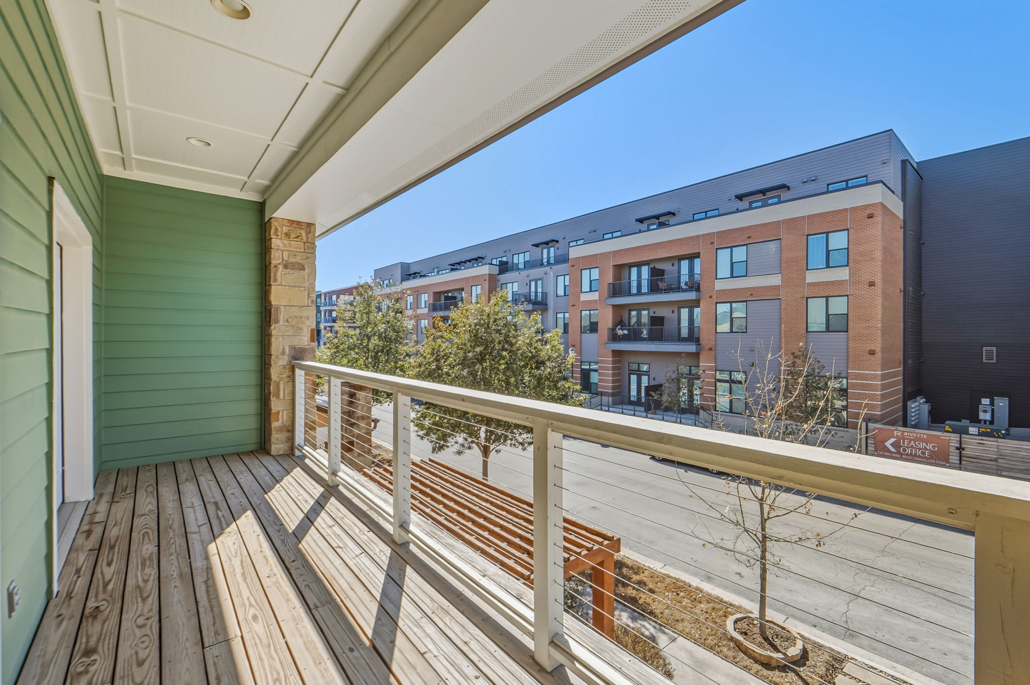 3919 Vaughan Street Austin, TX 78723 - Photo 39 of 40 A well-lit balcony features a wooden deck and a clean railing, overlooking a modern apartment building and street.