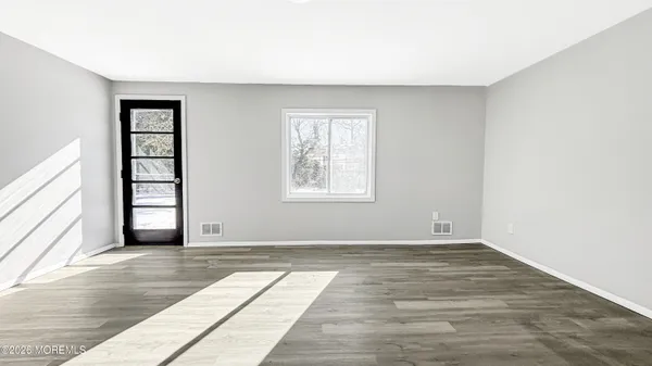 a view of an empty room with wooden floor and windows