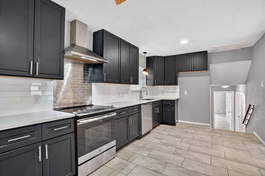 6609 Genoa Road Fort Worth, TX 76116 - Photo 17 of 40 Modern kitchen featuring dark cabinetry, white countertops, stainless steel appliances including a range hood and dishwasher, and a subway tile backsplash