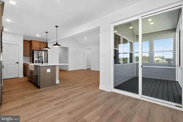 an empty room with wooden floor kitchen view and a window