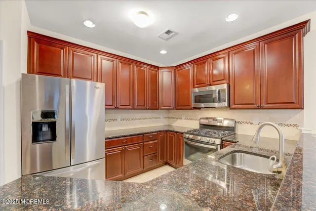 a kitchen with stainless steel appliances granite countertop a refrigerator a sink dishwasher a stove with wooden cabinets and floor