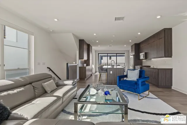 a living room with furniture kitchen view and a wooden floor