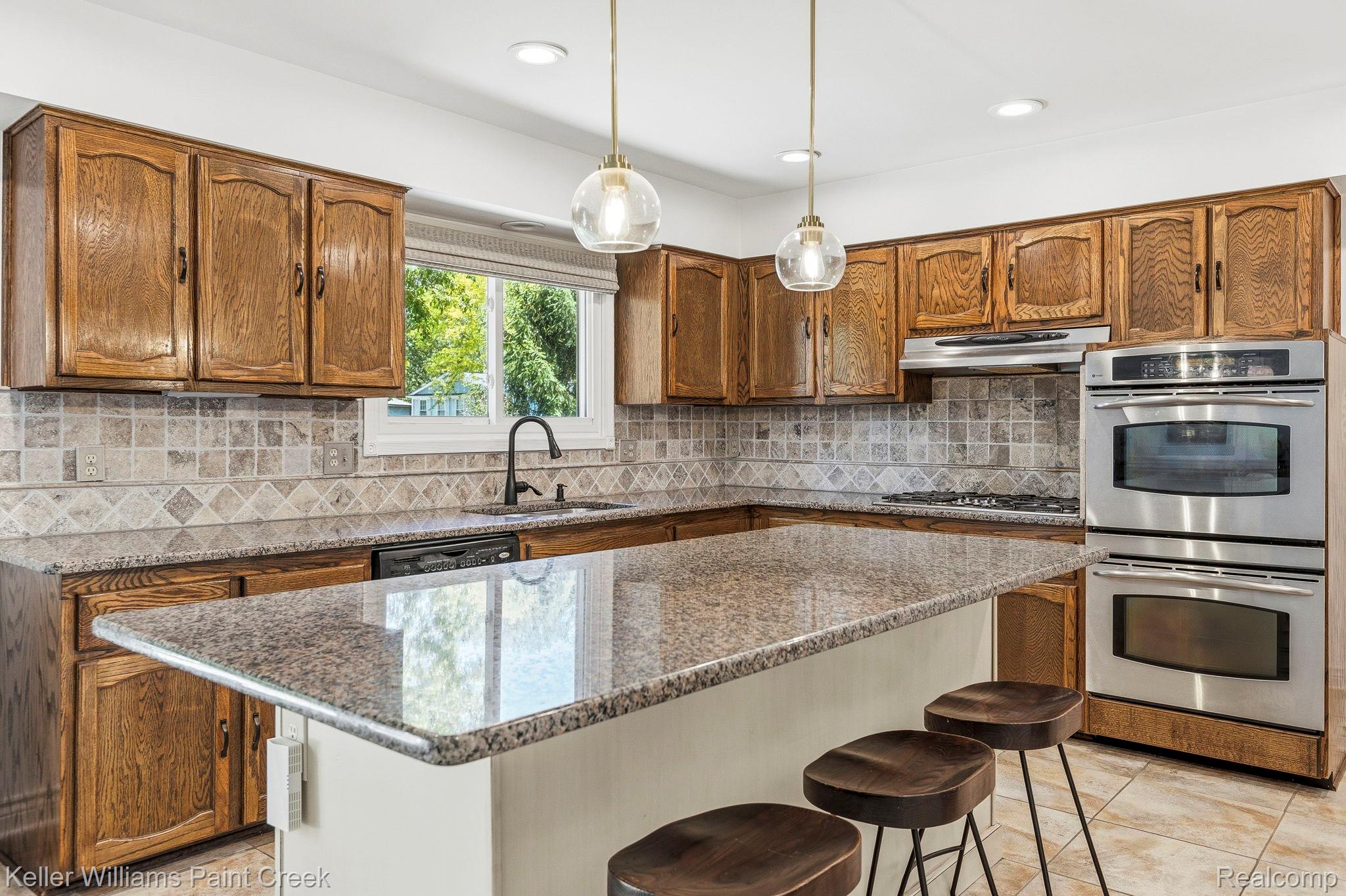 1675 North Kilburn Road Rochester, MI 48306 - Photo 26 of 48 Kitchen featuring a central island with a granite countertop, wood cabinetry, a tile backsplash, and stainless steel double ovens