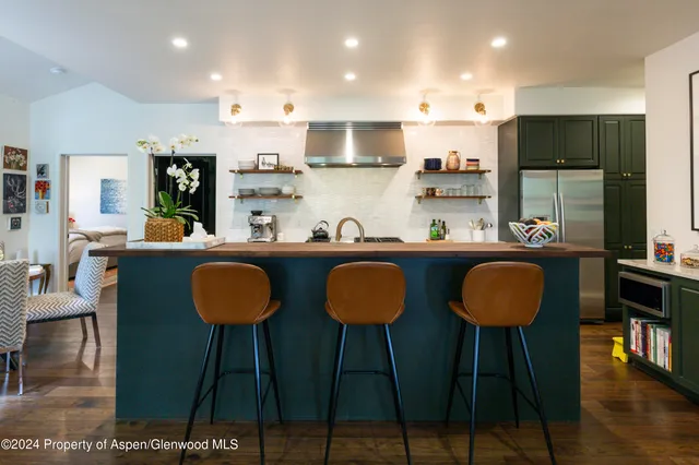 a kitchen with stainless steel appliances kitchen island granite countertop a dining table chairs refrigerator and sink