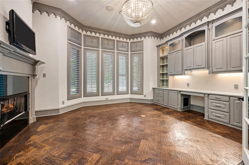 6900 Rockingham Court Colleyville, TX 76034 - Photo 13 of 40 Private office featuring a fireplace, custom built-in cabinetry with under-cabinet lighting, a chandelier, bay windows with plantation shutters, and patterned hardwood flooring