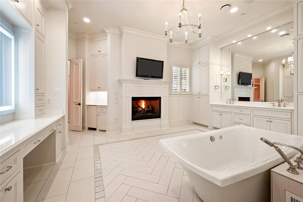 6900 Rockingham Court Colleyville, TX 76034 - Photo 17 of 40 Freestanding soaking tub with polished chrome fixtures, central fireplace, herringbone-patterned tile flooring, extensive built-in cabinetry, and a double vanity with an oversized mirror