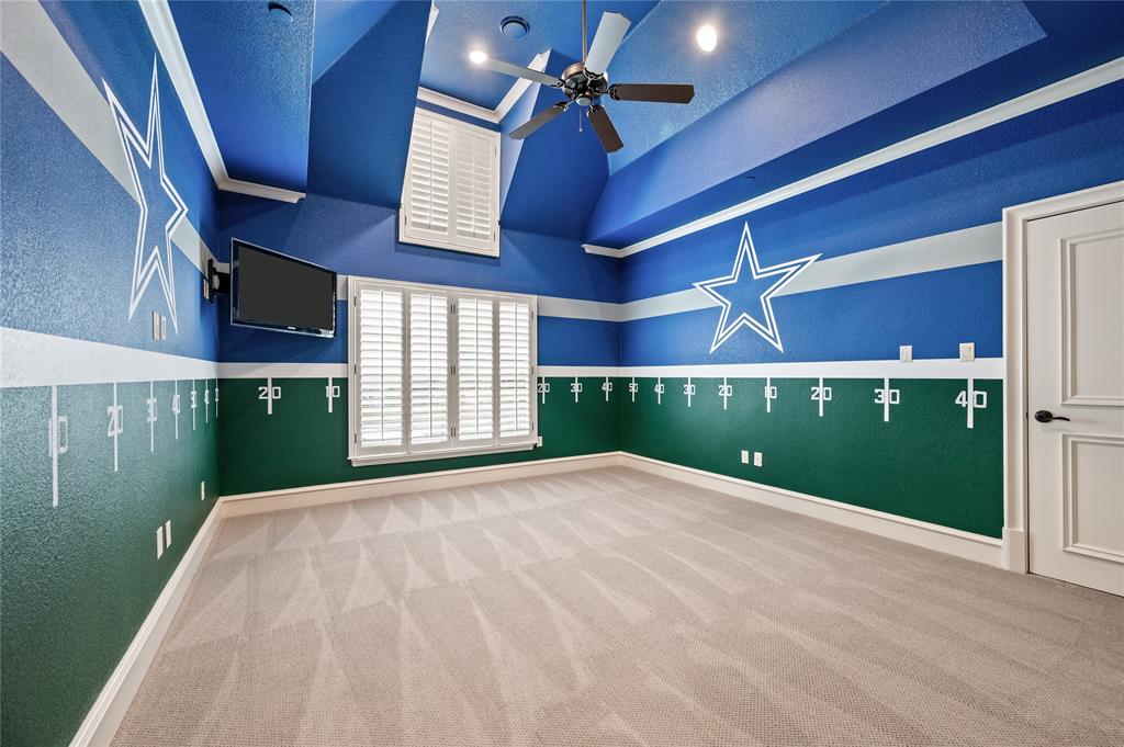 6900 Rockingham Court Colleyville, TX 76034 - Photo 21 of 40 Dallas Cowboys themed bedroom featuring vaulted ceilings, a ceiling fan with LED integrated lighting, two windows with white plantation shutters, and a paneled door with dark hardware, and ensuite bathroom.