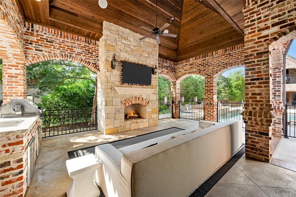 6900 Rockingham Court Colleyville, TX 76034 - Photo 32 of 40 Covered patio and outdoor kitchen off of main kitchen features a stone fireplace with a mounted television, a ceiling fan, BBQ Grill, Refrigerator, and a wood-paneled vaulted ceiling
