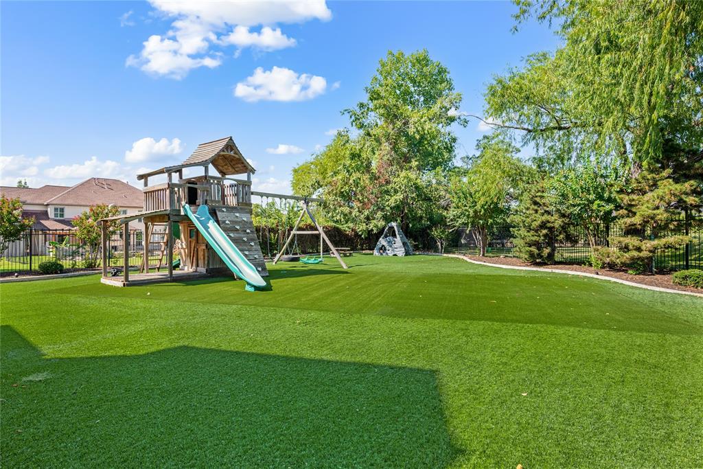 6900 Rockingham Court Colleyville, TX 76034 - Photo 37 of 40 Expansive play area with safety gate across from putting green features artificial turf, a multi-level wooden playset with slide and rock wall, and a separate swing set