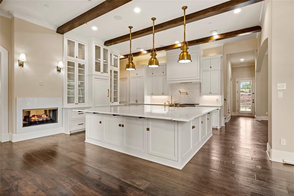 6900 Rockingham Court Colleyville, TX 76034 - Photo 10 of 40 Gourmet Chef's kitchen featuring a large central island with white cabinetry, wood flooring, exposed ceiling beams, and a modern fireplace, Sub Zero Refrigerator and Freezer, Updated Appliances, Dual Dishwashers