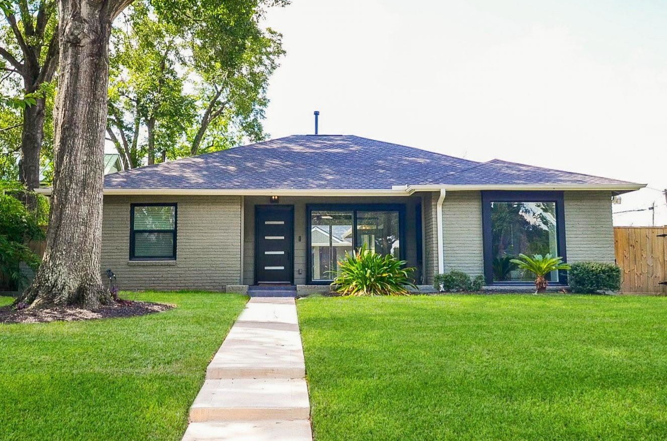 This charming complete remodeled single-story home features a clean, modern exterior with a light facade and a dark roof. It has a well-maintained front lawn with mature trees and shrubs, and a welcoming pathway leading to a sleek front door. Perfect for those seeking a cozy, stylish residence.
