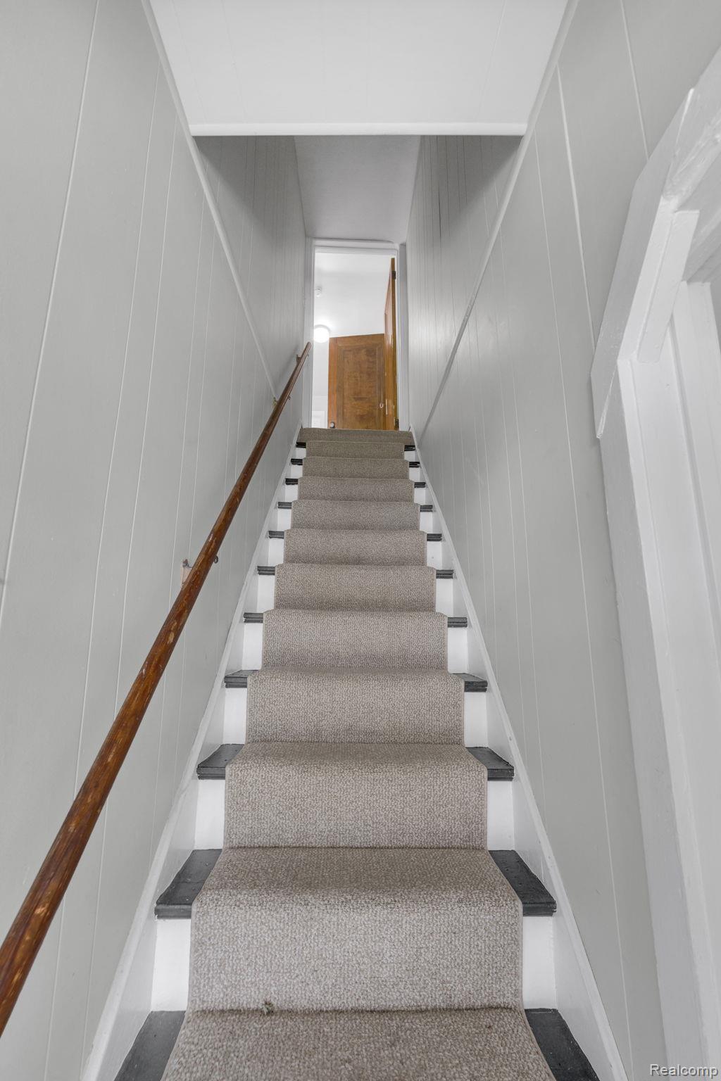 7631 Maple Street Dearborn, MI 48126 - Photo 29 of 48 Staircase featuring light gray carpet runner, dark risers, white stringers, light gray wall paneling, and a natural wood handrail