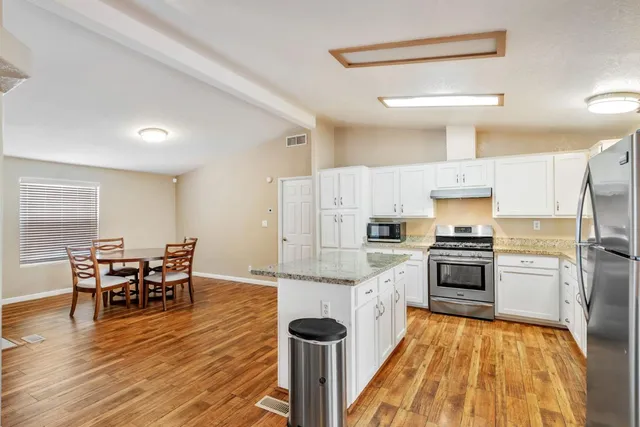 a kitchen with stainless steel appliances kitchen island granite countertop a table chairs stove and refrigerator
