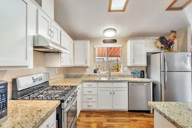 a kitchen with stainless steel appliances granite countertop a stove a refrigerator a sink dishwasher and white cabinets next to a window