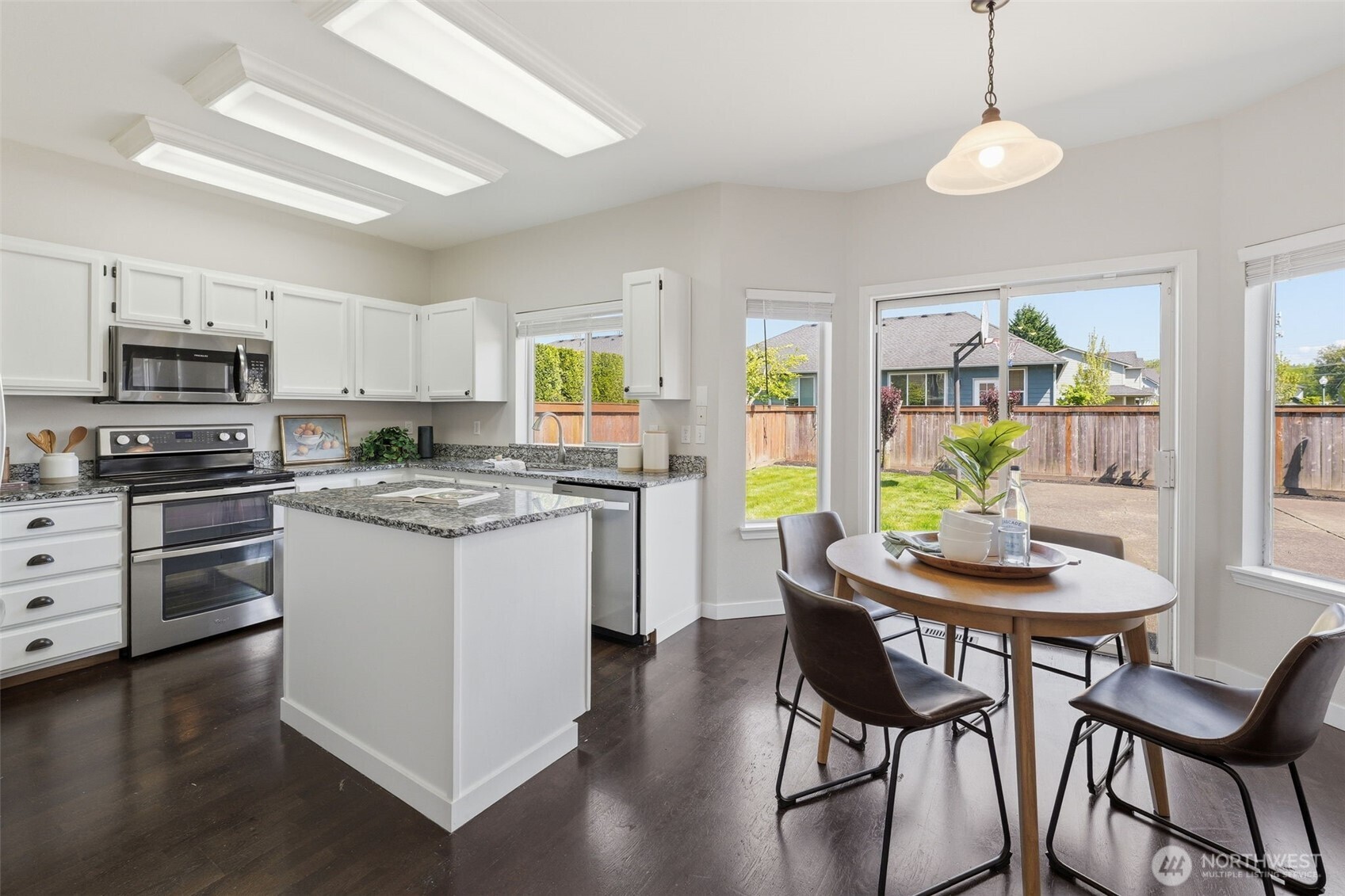 7625 148th Avenue East Sumner, WA 98390 - Photo 14 of 40 a kitchen with stainless steel appliances kitchen island granite countertop a stove a microwave a dining table and chairs with wooden floor