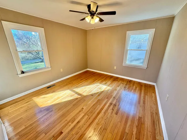 a view of an empty room with wooden floor and a ceiling fan