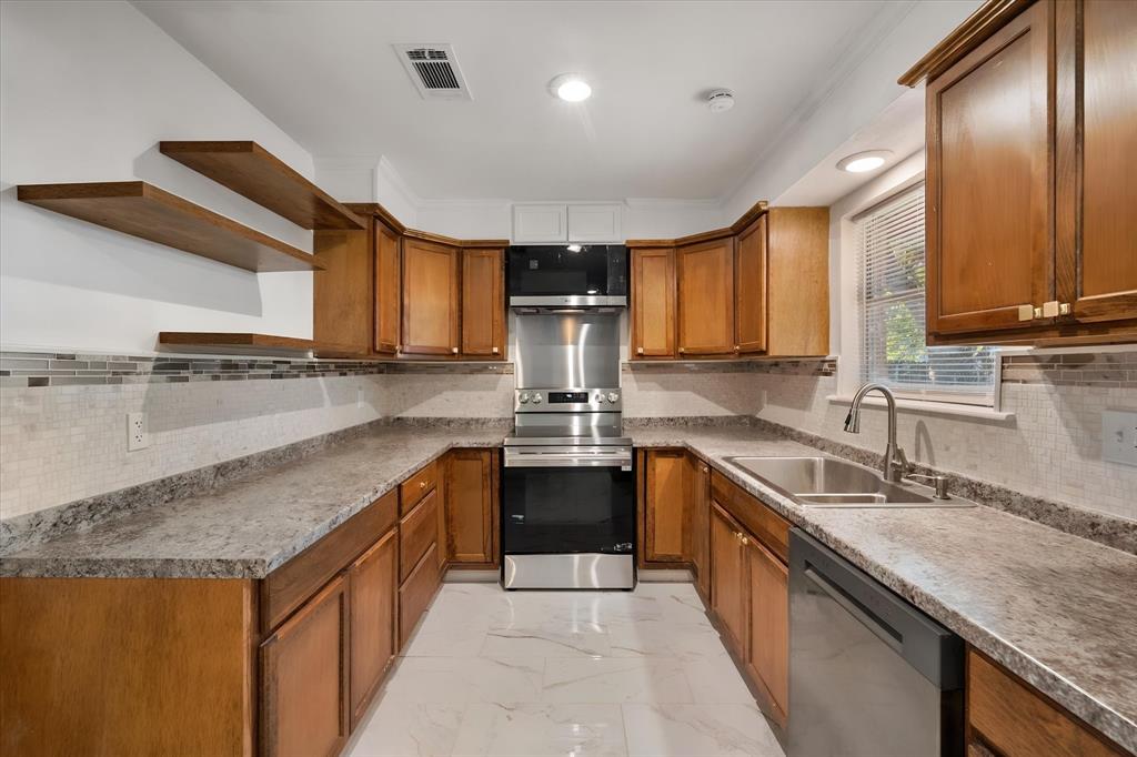 3400 Emhouse Road Corsicana, TX 75110 - Photo 23 of 34 U-shaped kitchen with wood-finish cabinetry, stainless steel appliances, mosaic tile backsplash, and light-toned countertops
